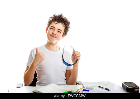 Acne Caucasian teenager makes success gesture with right thumb up holding black plastic 3D Cinema eyeglasses while doing homework Stock Photo