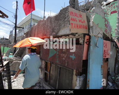 Manila, Philippines. 23rd June, 2015. A resident of Sarmiento Street walks past by a placard that reads, 'Bring back our homes,' as its community protests the demolition of its homes last June 16. Residents demanded the local government of Manila to halt the planned demolition of their homes, alleging that the projects planned for the place are alibis to accommodate a bus company owned by Guia Gomez, one of the many mistresses of Manila mayor Joseph Estrada. Credit:  Richard James Mendoza/Pacific Press/Alamy Live News Stock Photo