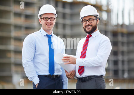Happy architects in helmets and formalwear having meeting outdoors Stock Photo