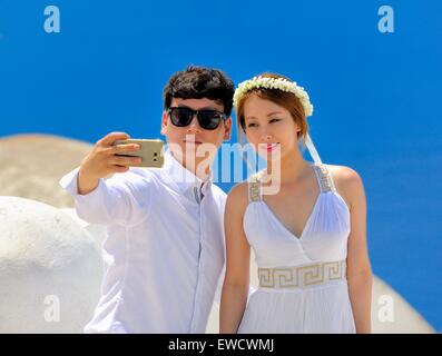 A young chinese couple taking a mobile phone selfie in their wedding outfits Oia Santorini Greece Stock Photo