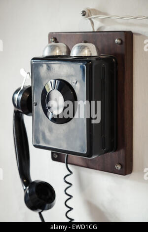 Vintage black wired phone hanging on old white wall, vintage toned photo with selective focus Stock Photo