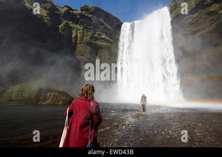 two female tourists pose for photographs at skogafoss waterfall in iceland Stock Photo