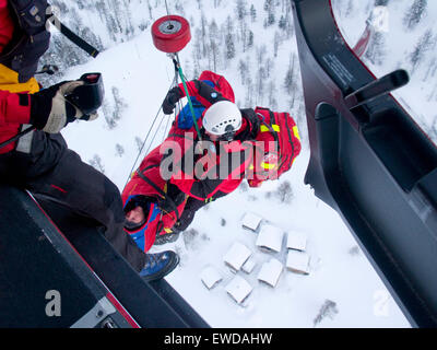 An emergency doctor and patient are being hoisted up to the rescue helicopter after a mountain accident. Stock Photo