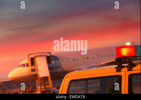 Detail of Follow-Me vehicle in front of aircraft, red sunset. Lot of blurring for copy space. Stock Photo