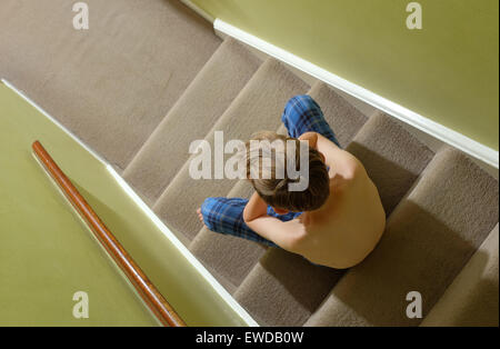 A child sitting on the stairs with his head in his hands looking upset