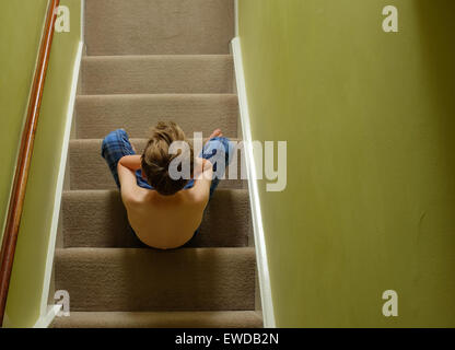 A child sitting on the stairs with his head in his hands looking upset Stock Photo