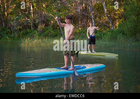 Two boys paddling stand up paddle boards on a small, secluded lake in Northern California. Stock Photo