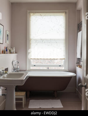 Free standing roll top bath in bathroom with wooden flooring and victorian style basin Stock Photo