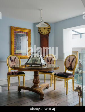 Three gilt dining chairs covered in Cory Visitorian hare head fabric round circular table in room with antique clock