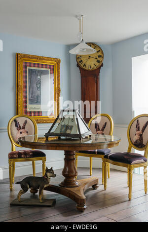 Three gilt dining chairs covered in Cory Visitorian hare head fabric round circular table in room with antique clock