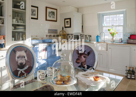 Dining chairs upholstered in Cory's Visitorian prints around glass topped dining table in kitchen with white dresser and aga