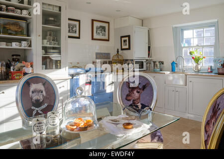 Dining chairs upholstered in Cory's Visitorian prints around glass topped dining table in kitchen with white dresser and aga