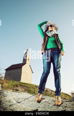 Young woman posing with stylish hat. Cowboy style. Old romanesque church Archangel Michael in Slovak republic.