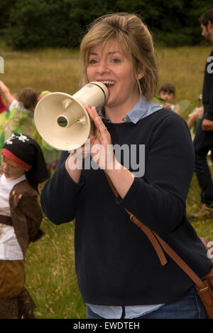 Young woman using megaphone to organise the crowds prior to a community summer parade, Frensham, Surrey, UK. Stock Photo