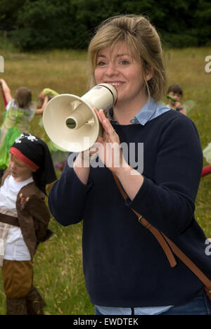 Young woman using megaphone to organise the crowds prior to a community summer parade, Frensham, Surrey, UK. Stock Photo