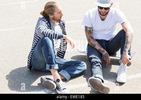 Two young men sitting on the ground, chatting Stock Photo