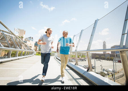 Two young men jogging along footbridge Stock Photo