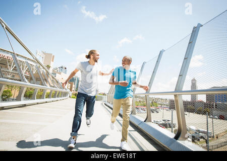 Two young men jogging along footbridge Stock Photo