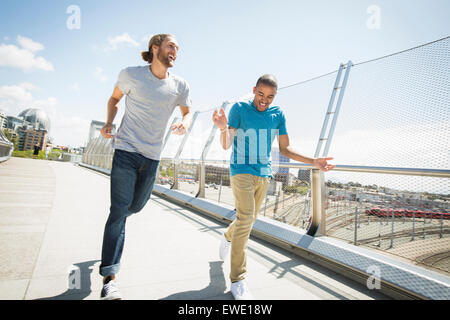 Two young men jogging along footbridge Stock Photo