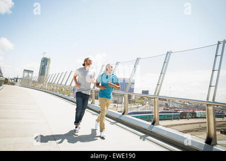 Two young men jogging along footbridge Stock Photo