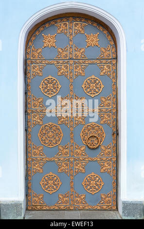 Vintage door with wrought golden ornament on a background of blue plastered walls. Stock Photo