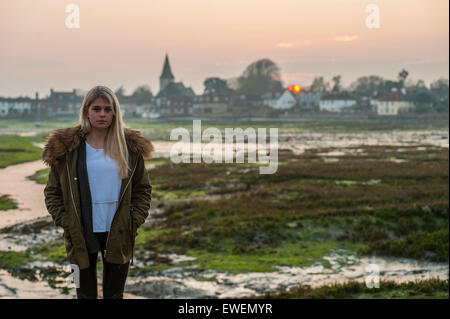 A pretty girl stands in front of a sunset over a quintessential English village Stock Photo