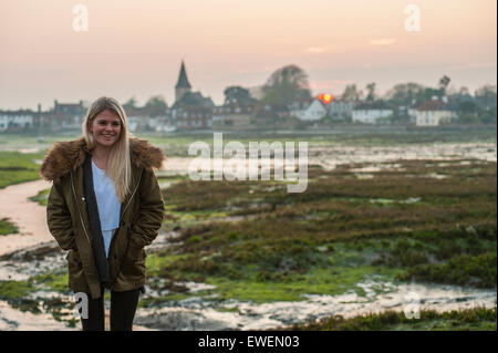 A pretty girl stands in front of a sunset over a quintessential English village Stock Photo