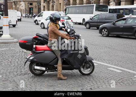Woman riding a motorcycle wearing cowboy boots and a protective apron in Paris, France Stock Photo