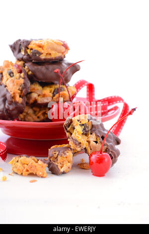 French style Florentine biscuits with whole maraschino cherries on red plate stand on white shabby chic table. Stock Photo