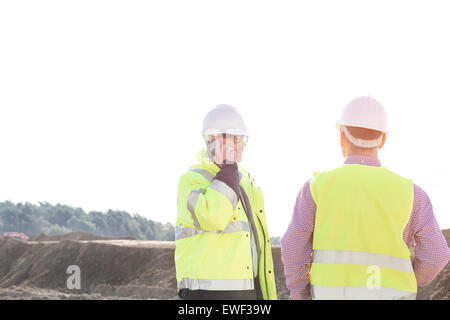 Male engineer using mobile phone while standing with colleague at construction site against clear sky Stock Photo