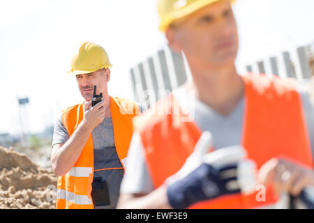 Middle-aged male worker using walkie-talkie with colleague in foreground at construction site Stock Photo