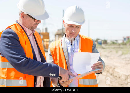 Engineers examining documents on clipboard at construction site against clear sky Stock Photo