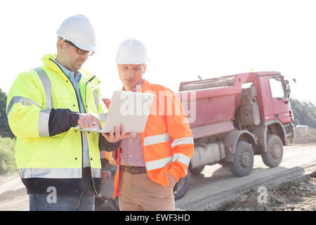 Engineers using laptop at construction site against clear sky on sunny day Stock Photo