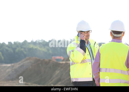 Supervisor using mobile phone while standing with colleague at construction site against clear sky Stock Photo
