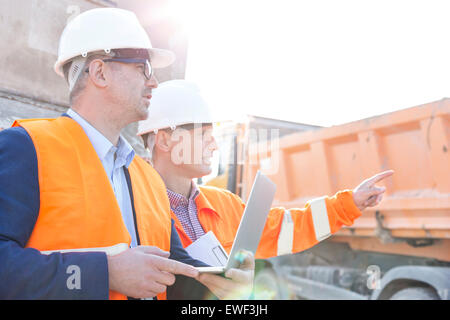 Supervisor showing something to colleague holding laptop at construction site