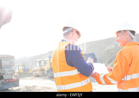 Happy engineers discussing over clipboard at construction site against clear sky Stock Photo