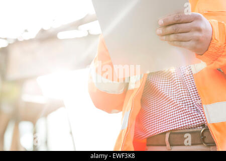 Midsection supervisor holding clipboard at construction site on sunny day Stock Photo