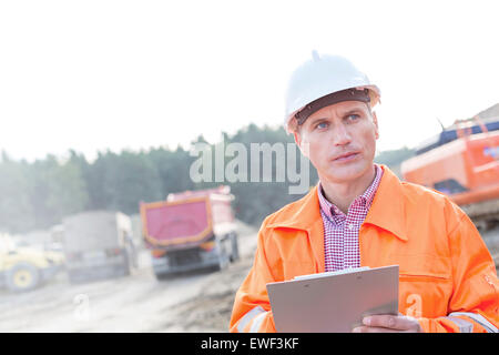 Engineer looking away while holding clipboard against clear sky Stock Photo
