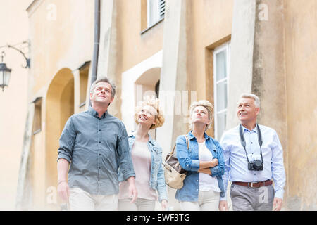 Smiling friends looking up while walking by building Stock Photo