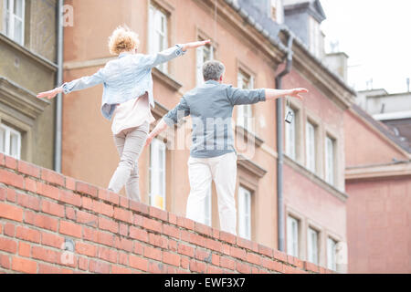 Rear view of middle-aged couple with arms outstretched walking on brick wall Stock Photo
