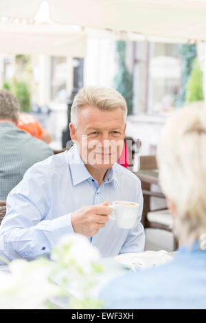 Smiling middle-aged man having coffee with woman at sidewalk cafe Stock Photo