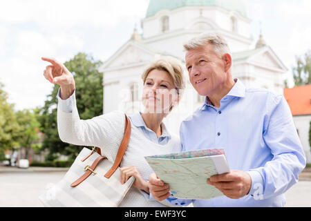 Middle-aged woman showing something to man holding map outdoors Stock Photo
