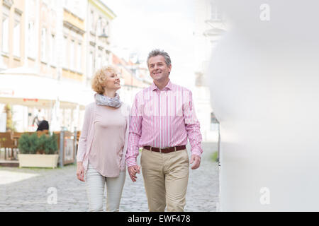 Happy middle-aged couple talking while walking in city Stock Photo