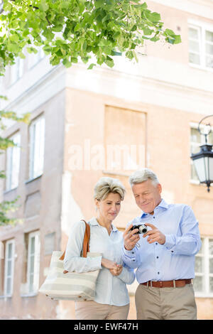 Middle-aged couple reviewing photos on digital camera outside building Stock Photo