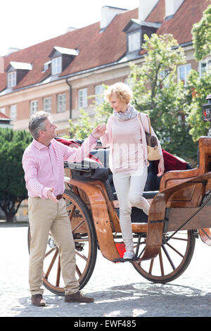 Full-length of middle-aged man assisting woman out of horse cart Stock Photo