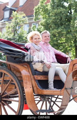Smiling middle-aged couple sitting in horse cart on city street Stock Photo