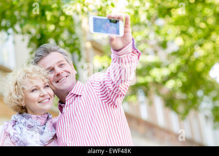 Happy middle-aged couple taking selfie through mobile phone outdoors Stock Photo