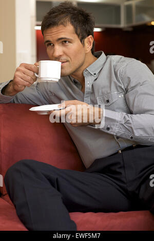 Young man drinking tea, sitting in sofa Stock Photo