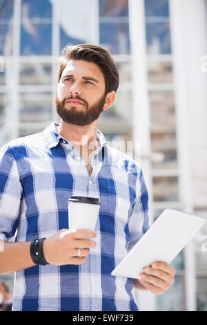 Thoughtful man looking away while holding disposable cup and tablet PC in city Stock Photo