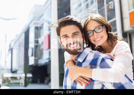 Portrait of happy man giving piggyback ride to woman in city Stock Photo